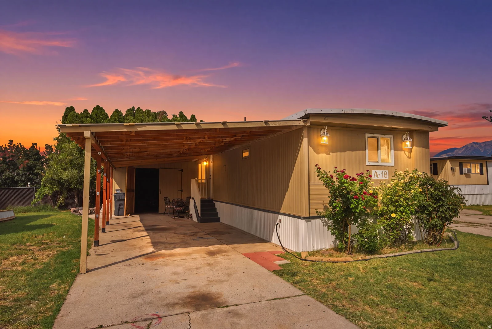 Single-story residence featuring a carport, exterior sconce lighting, and a manicured lawn